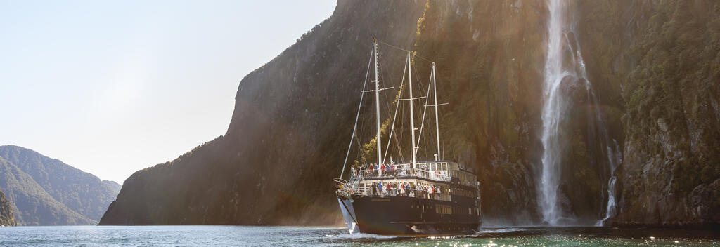 Scenic boat cruise in Milford Sound with spectacular waterfall backdrop