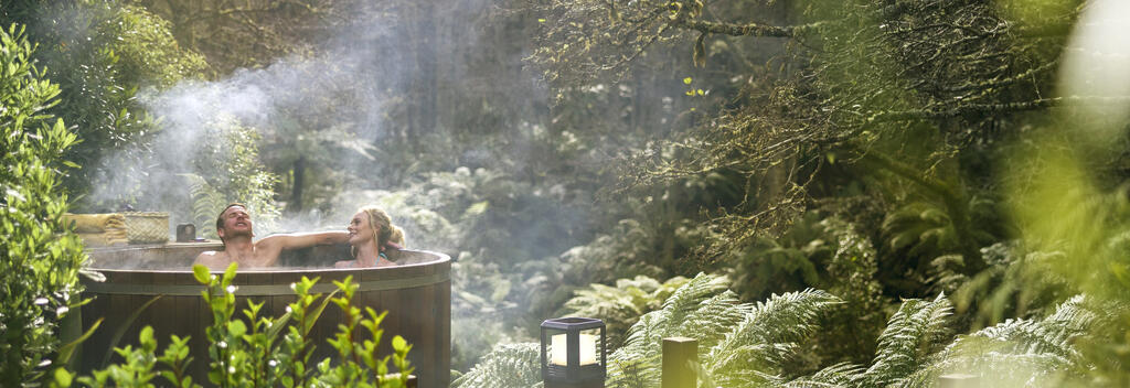 Couple soaking in a hot tub surrounded by lush green canopy in Rotorua, New Zealand