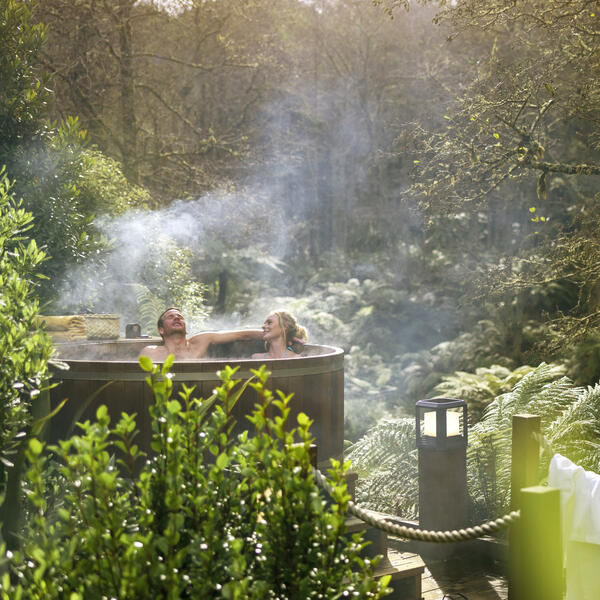 Couple soaking in a hot tub surrounded by lush green canopy in Rotorua, New Zealand