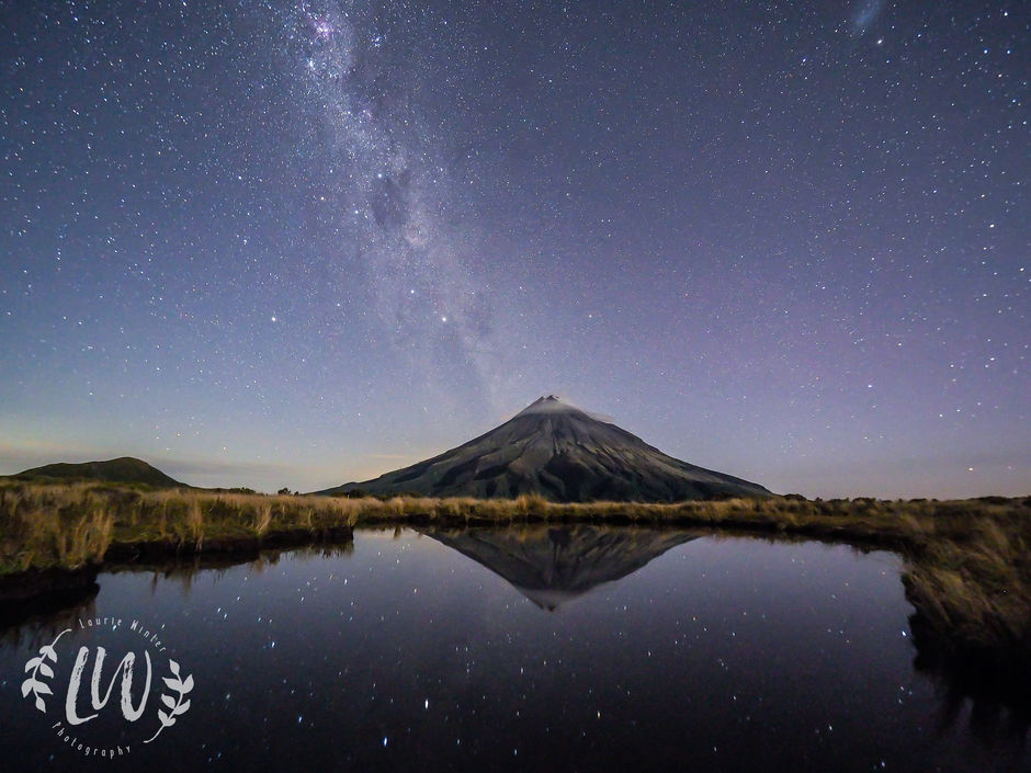 Looking across Pouakai Tarn towards Taranaki Maunga at night. Beautiful starscapes are reflected in the water.