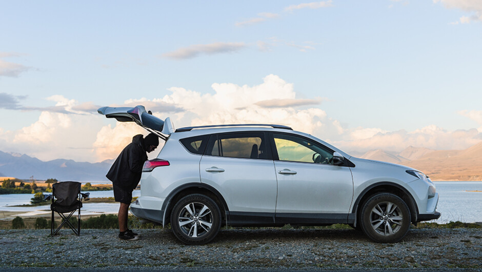 Man rummaging through boot of his GO Rentals car, getting ready for a camping trip.