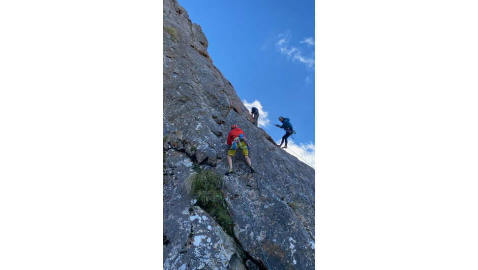 Group of rock climbers on a steep rock climbing face outdoors testing their limits in a safely set up environment.